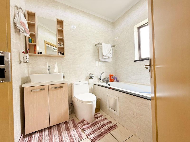 A well-maintained bathroom featuring a vessel sink vanity, wall-mounted mirror cabinet, toilet, and a bathtub with tiled finishes throughout.