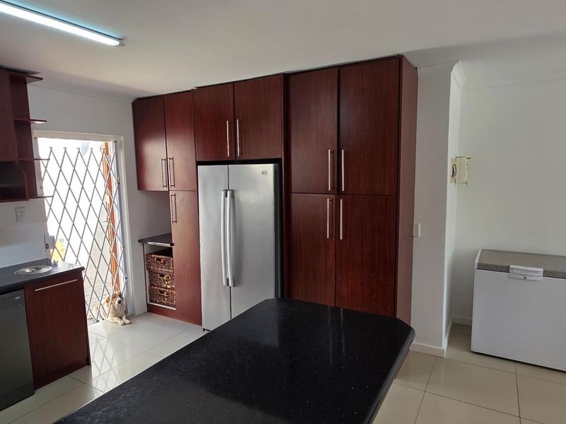 A functional kitchen featuring dark wood cabinetry, black granite countertops, tiled flooring, and integrated appliances with direct access to an exterior security gate.
