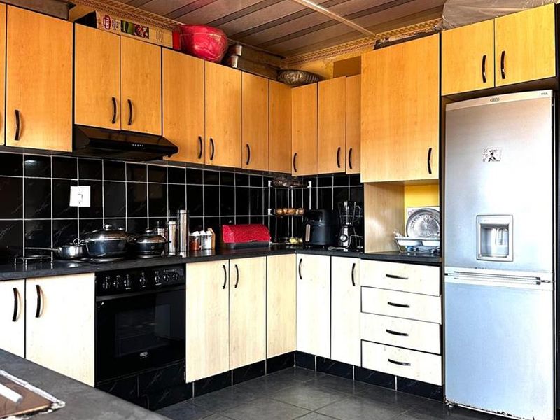 A functional kitchen featuring light wood-tone cabinetry, black tiled backsplash, dark countertops, and integrated appliances, offering a practical layout for daily use.