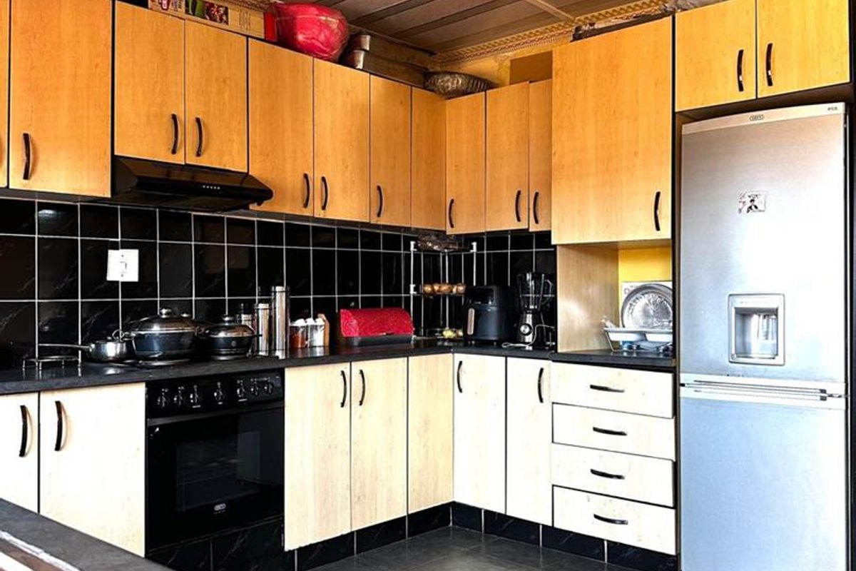 A functional kitchen featuring light wood-tone cabinetry, black tiled backsplash, dark countertops, and integrated appliances, offering a practical layout for daily use.