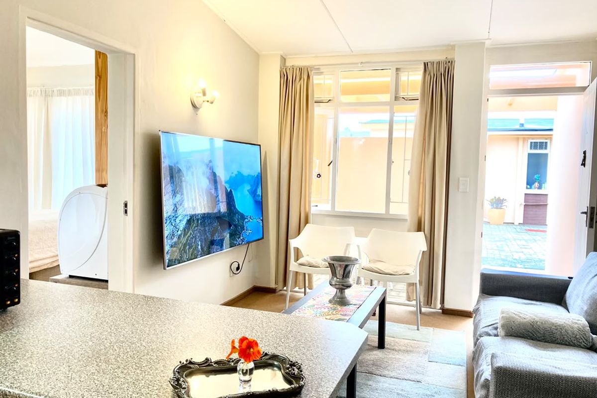 Open-plan living area featuring a granite kitchen countertop, wall-mounted television, and direct access to an outdoor patio area through a glass door.