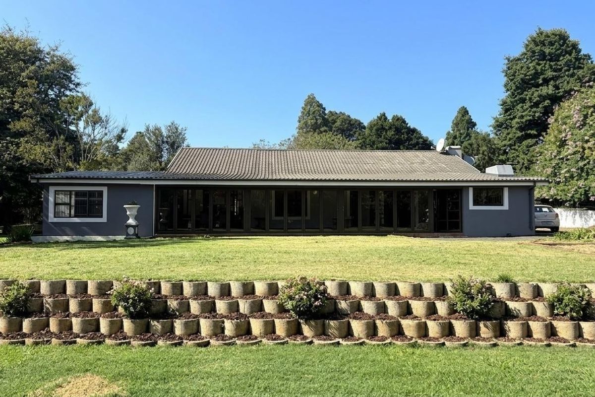 A well-maintained single-story residence featuring a tiled roof, dark-framed folding glass doors, and a landscaped rear garden with tiered concrete retaining walls.