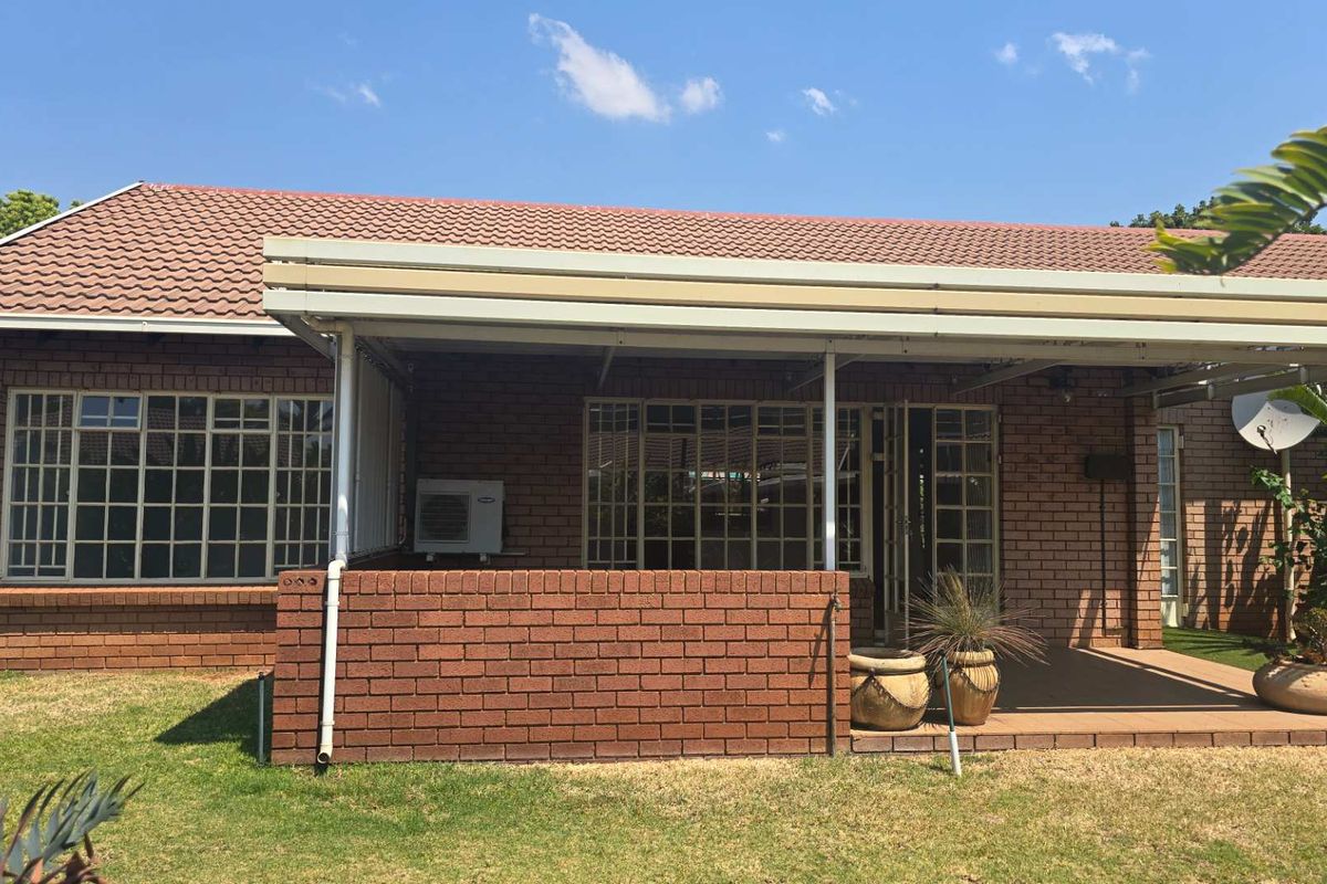 A well-maintained rear exterior view featuring a brick facade, tiled roof, and a covered patio area with security bars on the windows.