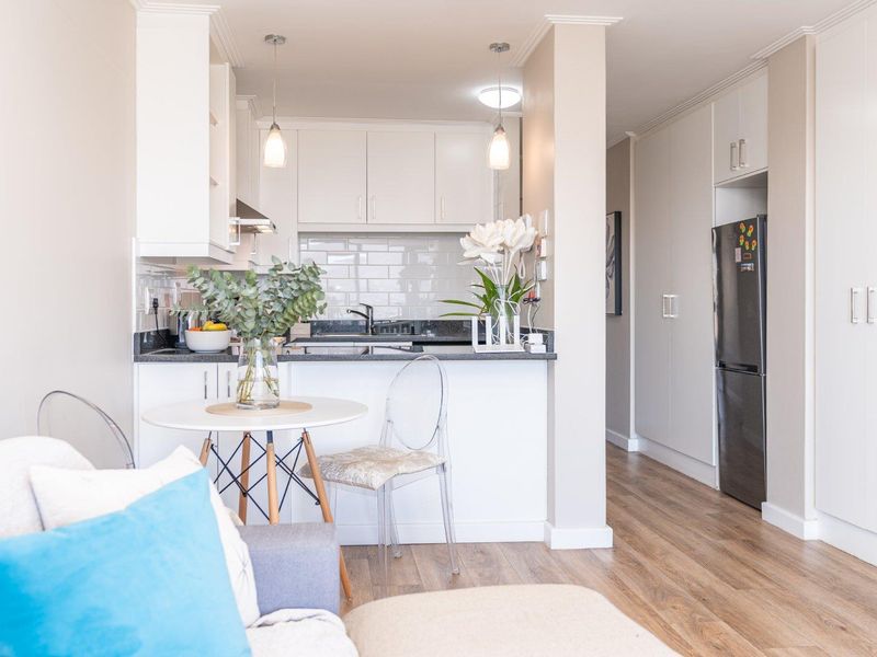 Modern open-plan kitchen featuring white cabinetry, stone countertops, subway tile backsplash, and integrated storage, seamlessly flowing into the living area.