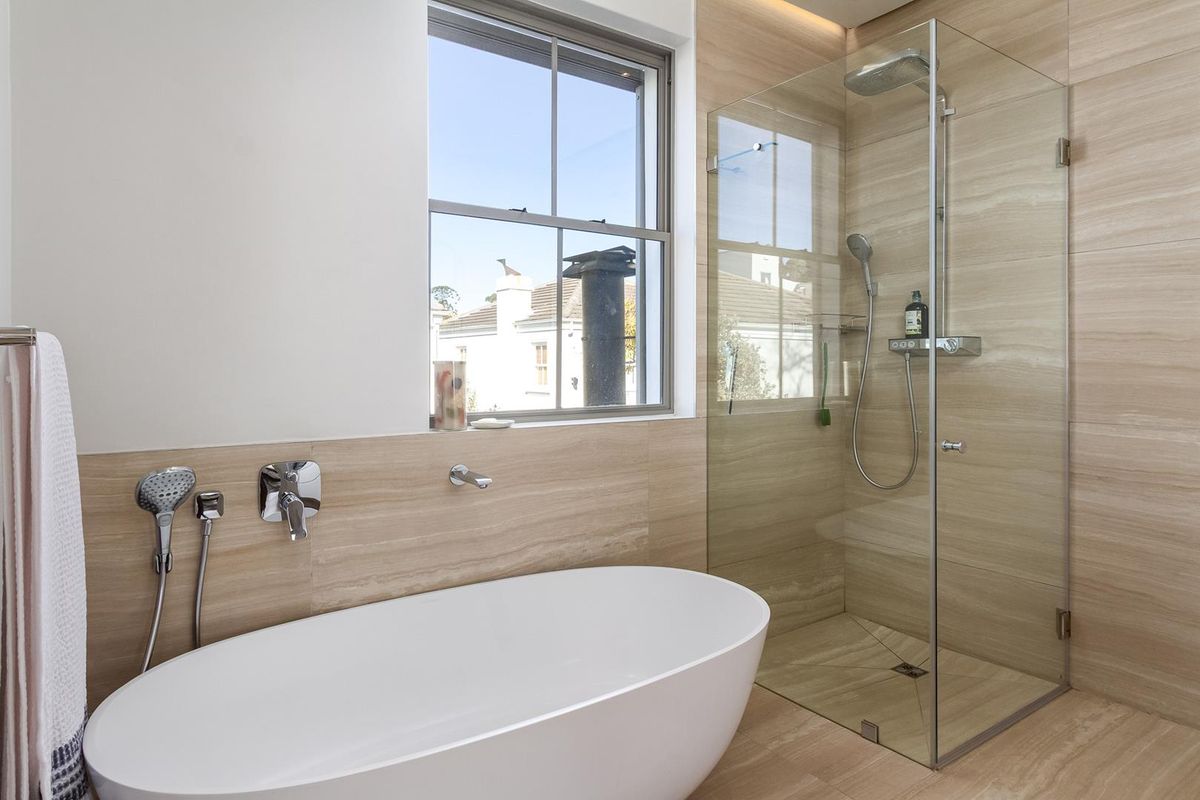 Modern bathroom featuring a sleek freestanding bathtub, a spacious walk-in shower with glass enclosure, and elegant travertine tiling throughout.