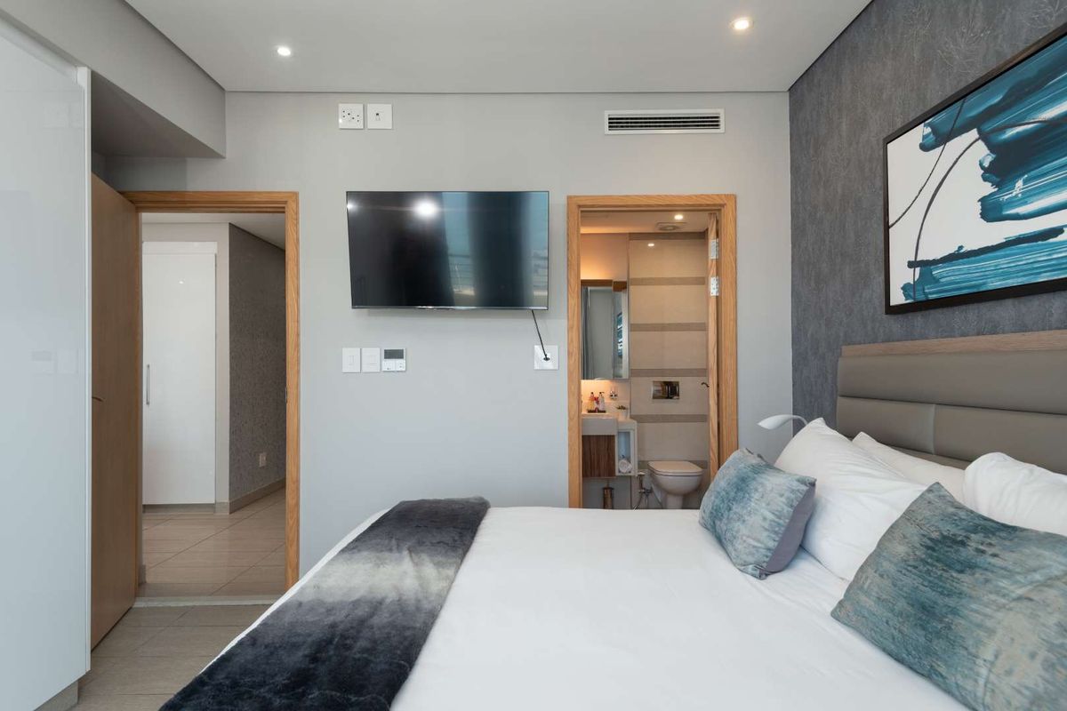 Modern bedroom featuring a neutral color palette, recessed ceiling lighting, integrated air conditioning vent, and an en-suite bathroom access.