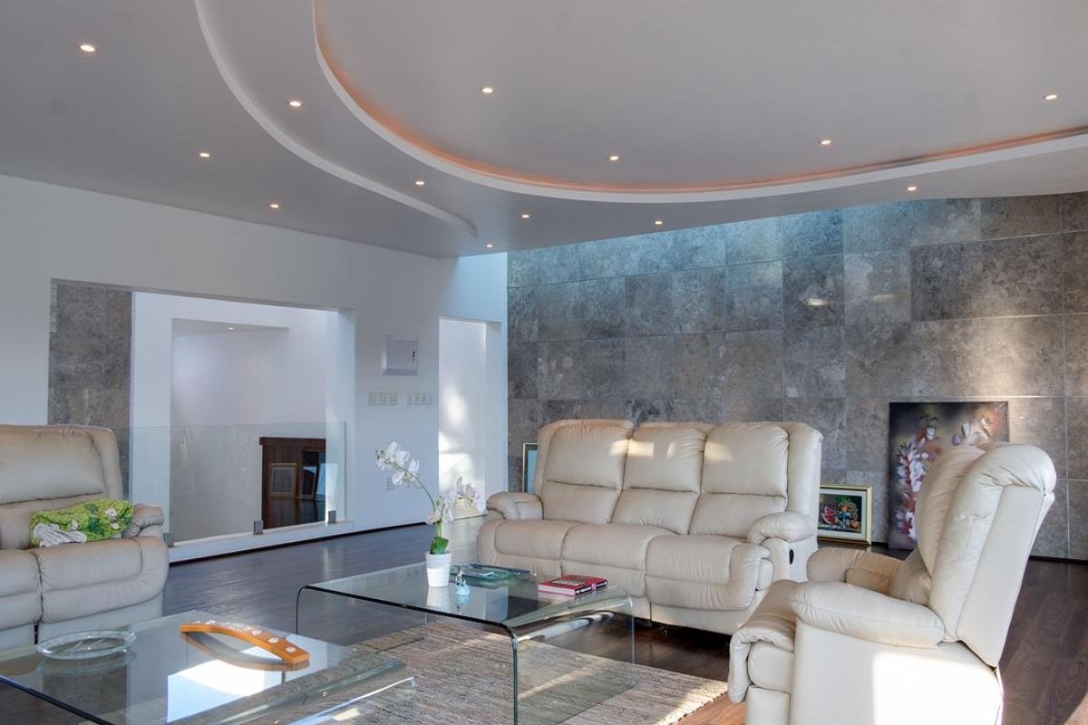 Spacious living room featuring a unique circular recessed ceiling with integrated lighting and a striking floor-to-ceiling stone feature wall.