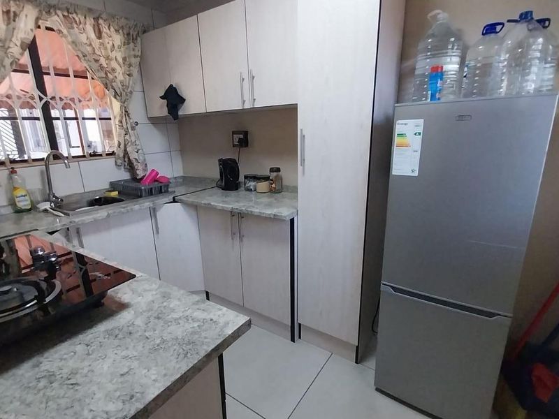 A functional kitchen featuring laminate countertops, built-in cabinetry, a gas hob, and a stainless steel sink with security bars on the window.
