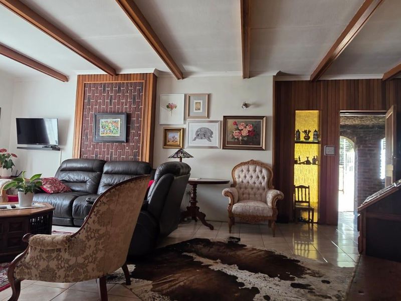 Spacious living room featuring exposed timber ceiling beams, wood paneling accents, tiled flooring, and a built-in display niche.