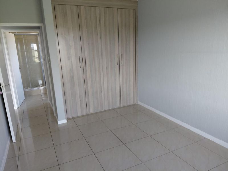 A clean, empty bedroom featuring modern light wood-finish built-in cupboards, neutral tiled flooring, and direct access to an en-suite bathroom.