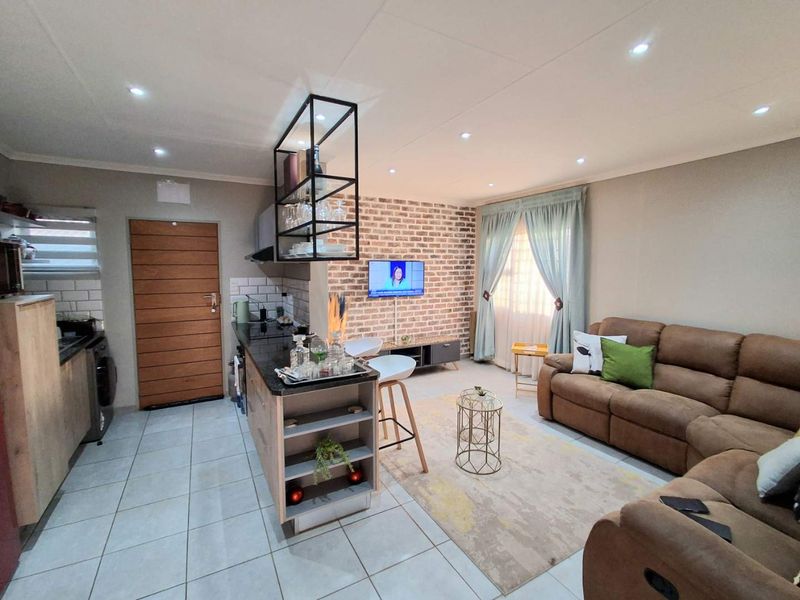 Open-plan living area featuring a modern kitchen island, exposed brick feature wall, and tiled flooring, creating a cohesive and functional living space.