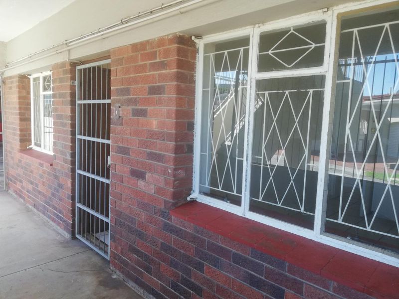 Exterior view of an apartment entrance featuring brick facade construction, security gates, and window security bars.