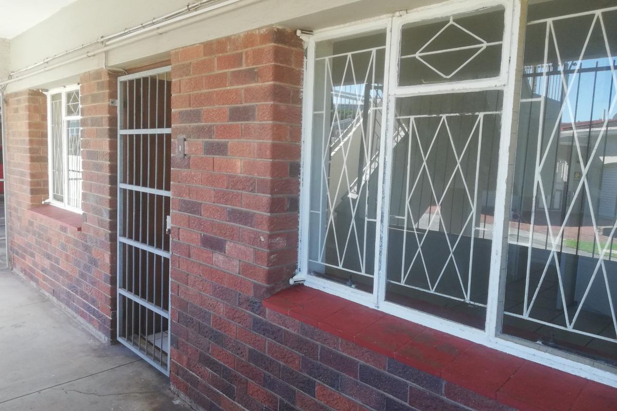 Exterior view of an apartment entrance featuring brick facade construction, security gates, and window security bars.