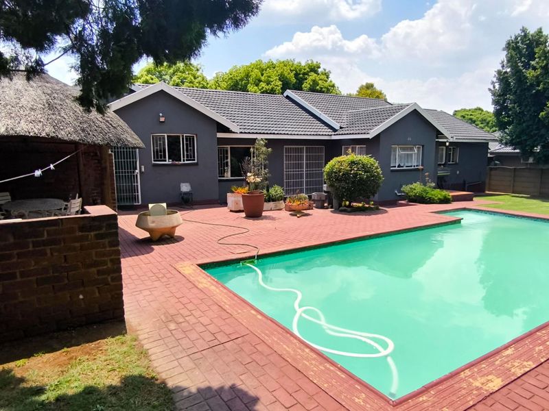 Rear exterior view featuring a swimming pool, brick paved patio area, and a traditional thatched lapa structure.