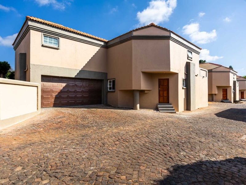 Front elevation of a multi-story residential property featuring a double garage, cobblestone driveway, and neutral exterior finish.