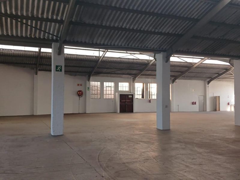 Spacious industrial warehouse area featuring high ceilings with exposed steel trusses, concrete flooring, and functional emergency exit infrastructure.