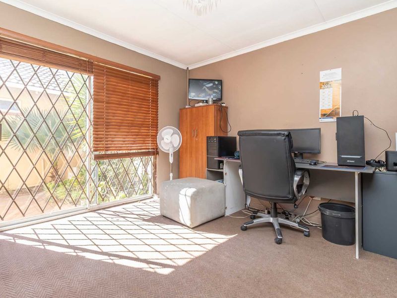 A functional home office space featuring carpeted flooring and a large sliding glass door with security gate providing access to the exterior.