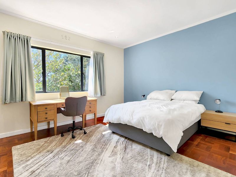 A bright and spacious bedroom featuring warm parquet flooring, a large window providing natural light, and a feature wall.