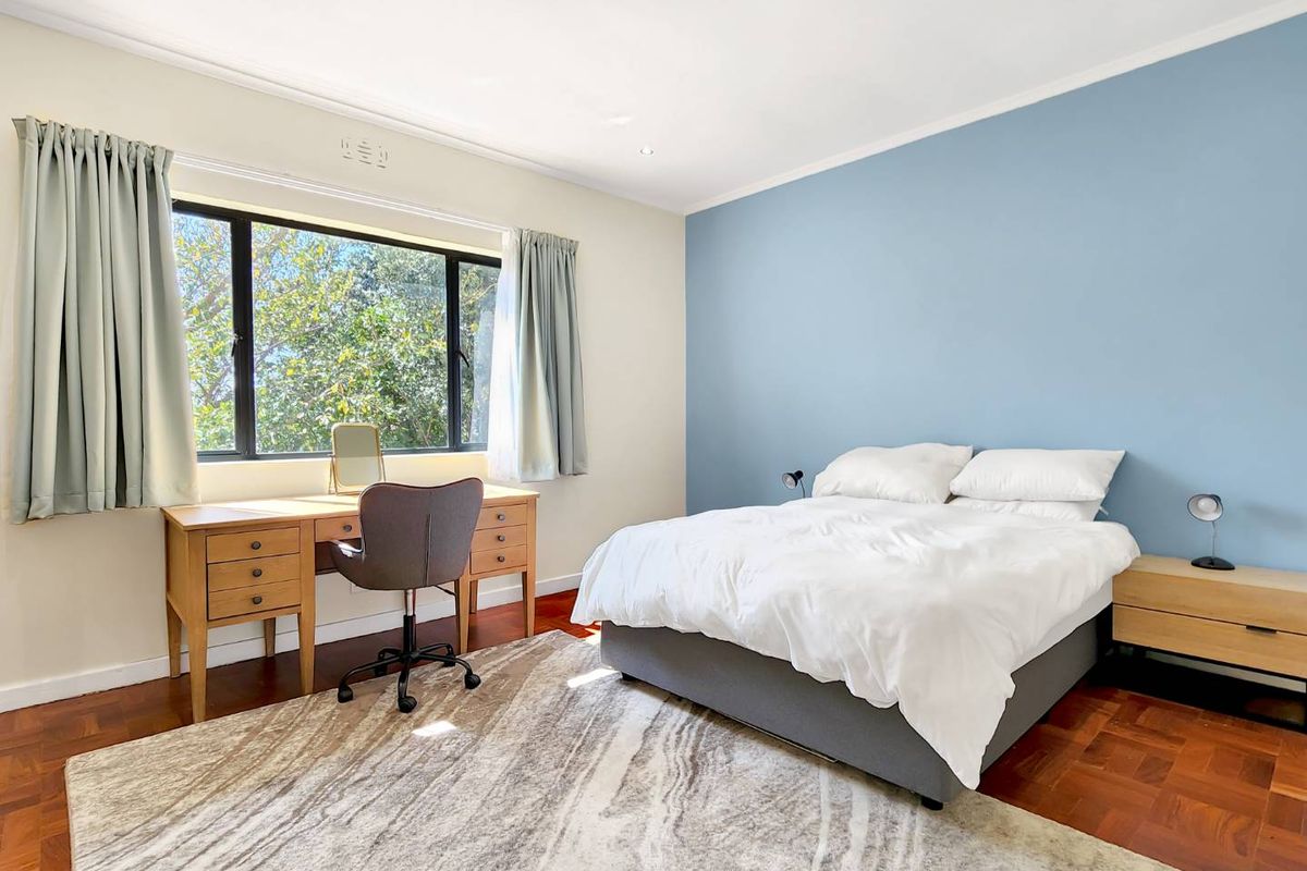 A bright and spacious bedroom featuring warm parquet flooring, a large window providing natural light, and a feature wall.