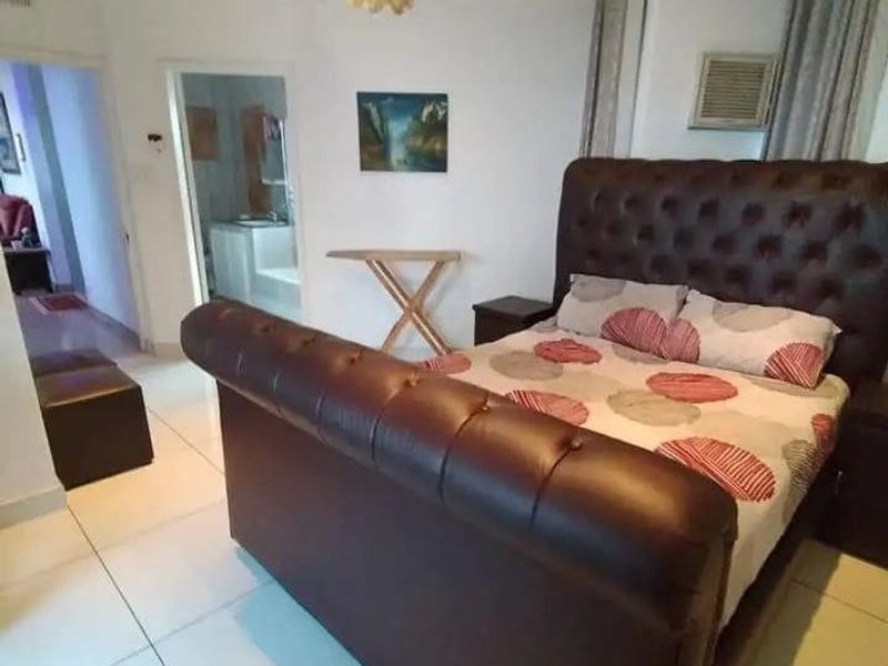 A spacious bedroom featuring large format floor tiles, recessed lighting, and an integrated air conditioning unit, with direct access to an adjoining bathroom.