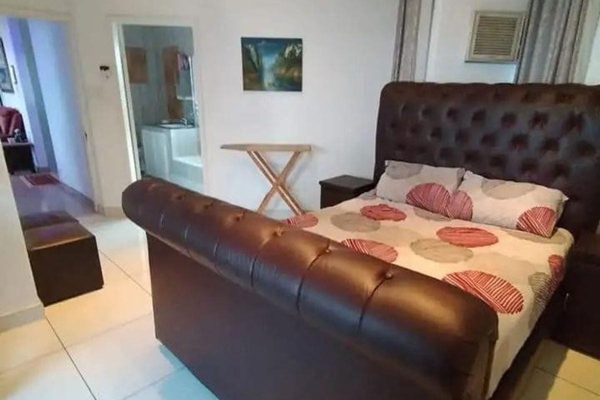 A spacious bedroom featuring large format floor tiles, recessed lighting, and an integrated air conditioning unit, with direct access to an adjoining bathroom.
