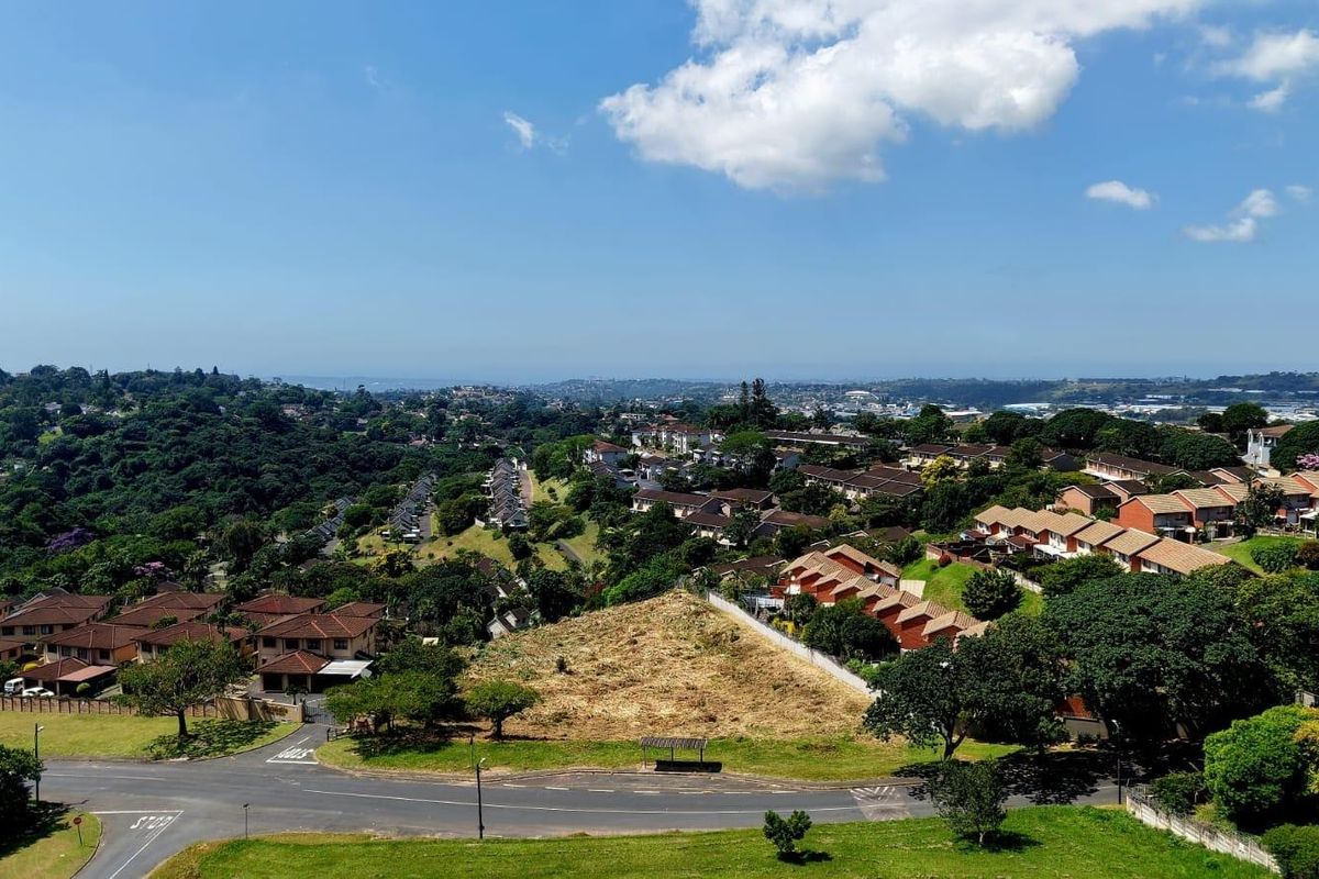An elevated aerial view of a vacant residential land plot situated within an established suburban neighborhood with surrounding housing and road infrastructure.
