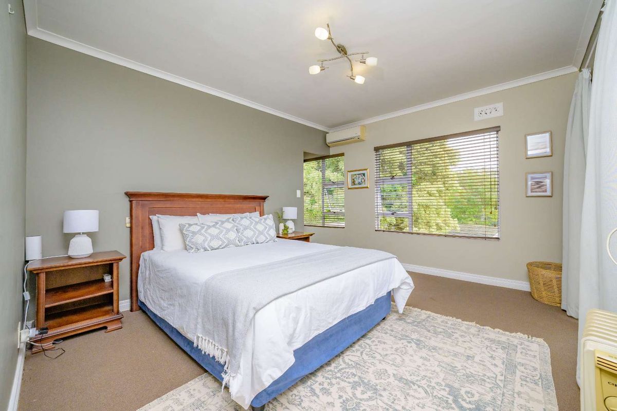 A well-maintained bedroom featuring neutral wall tones, carpeted flooring, split-system air conditioning, and large windows with venetian blinds.