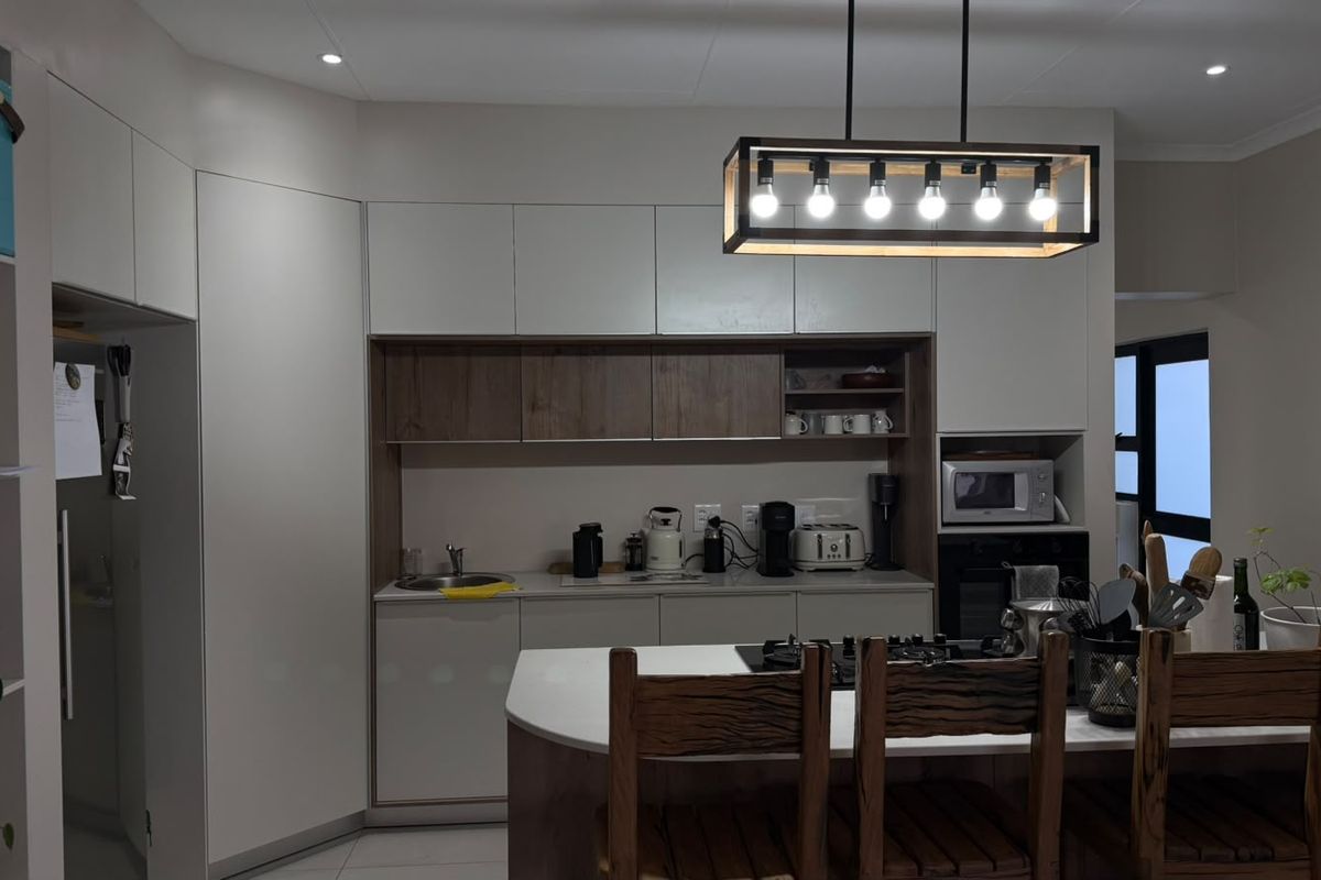 Modern kitchen featuring sleek two-tone cabinetry, a central island with a gas hob, built-in appliances, and stylish pendant lighting.