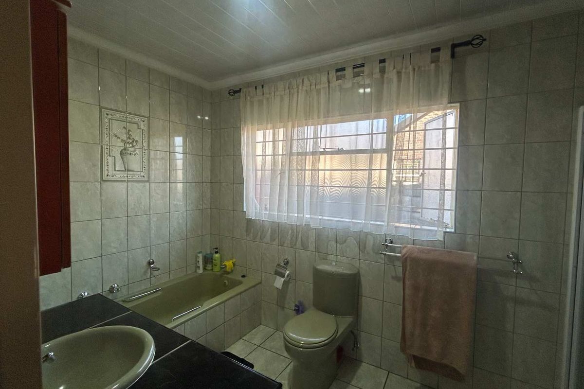 A functional bathroom featuring a built-in bathtub, toilet, and vanity basin with tiled finishes throughout.