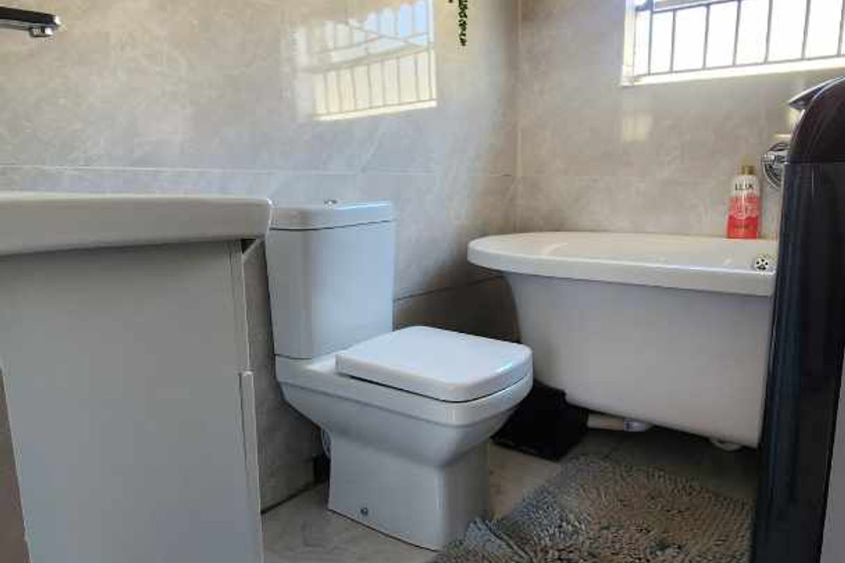 A modern bathroom featuring a freestanding bathtub, a sleek toilet, and wall-mounted shelving, finished with large-format marble-look tiles.