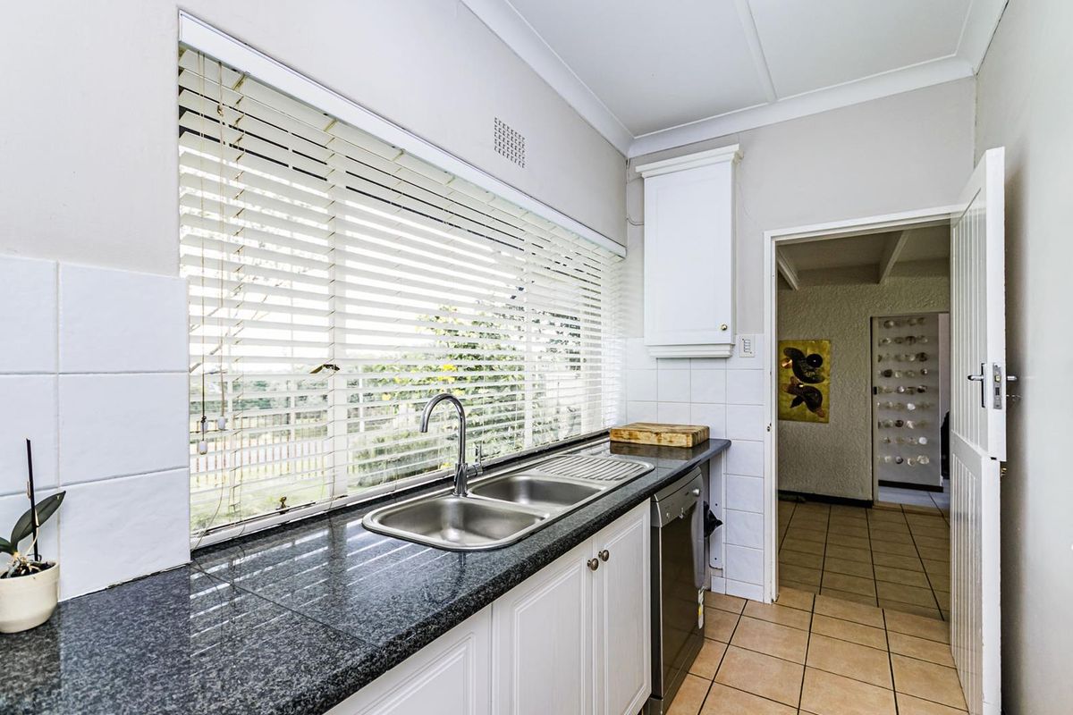 A functional kitchen featuring dark granite countertops, a double stainless steel sink, white cabinetry, and tiled flooring with a view through the window.