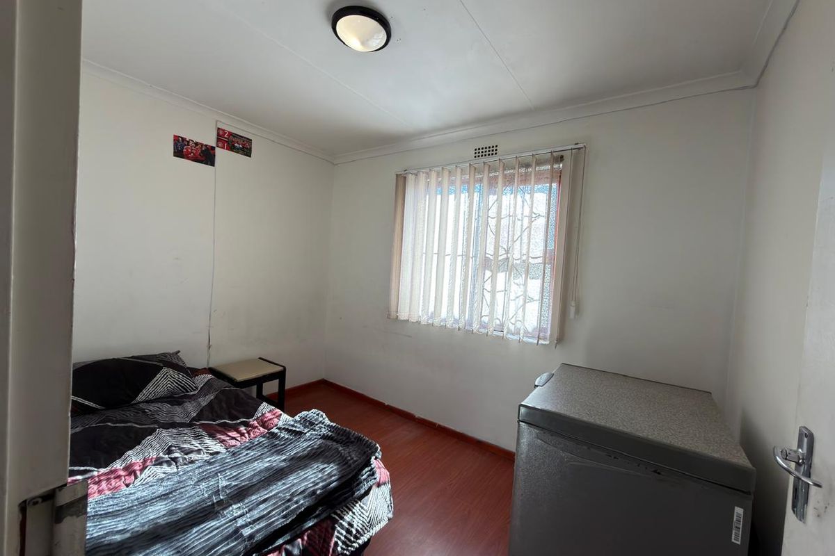 A bedroom featuring laminate flooring, vertical blinds, and a ceiling light fixture. The room requires cosmetic updates to the wall finishes.