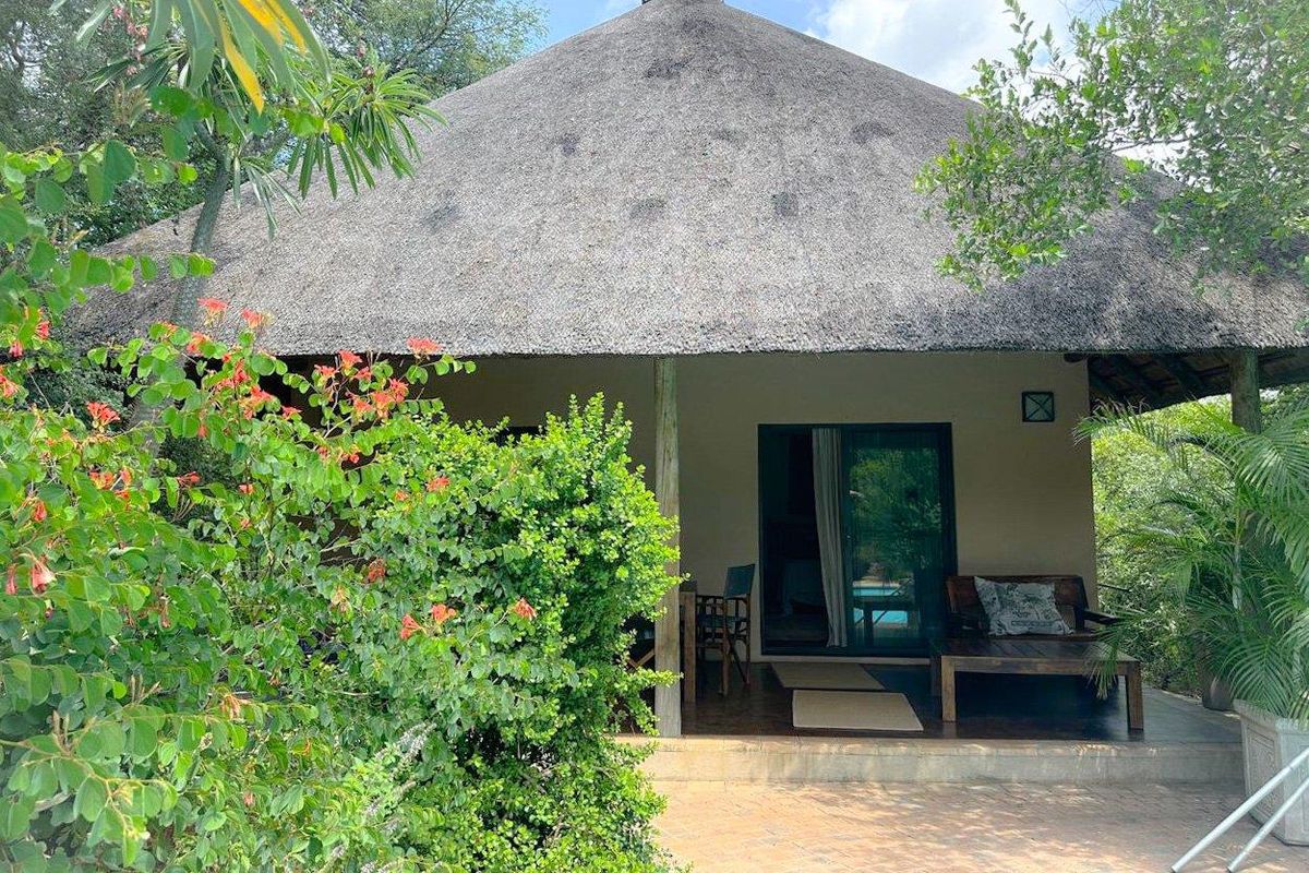 A charming cottage featuring a traditional thatched roof, a covered patio area, and lush surrounding garden greenery.