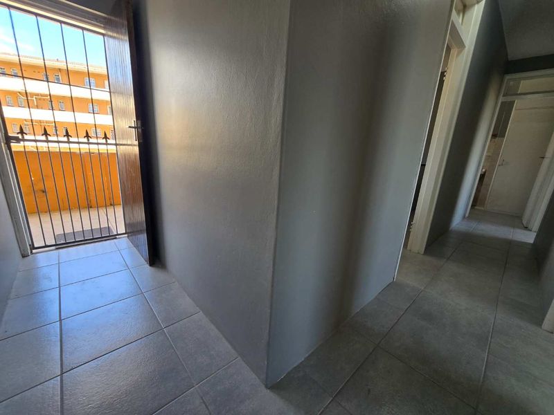 A clean, tiled hallway area featuring a security gate leading to an outdoor balcony and access to adjacent rooms.