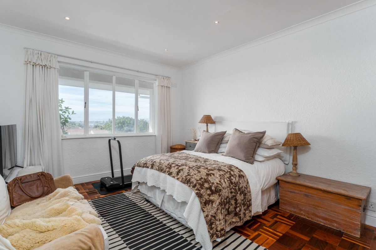A bright bedroom featuring classic parquet flooring, large windows with natural light, and recessed ceiling lighting.