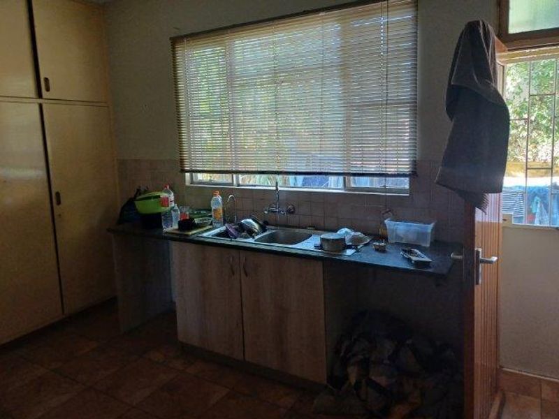A dated kitchen area featuring built-in cabinetry, a stainless steel sink, and tiled backsplash, offering potential for modernization and renovation.