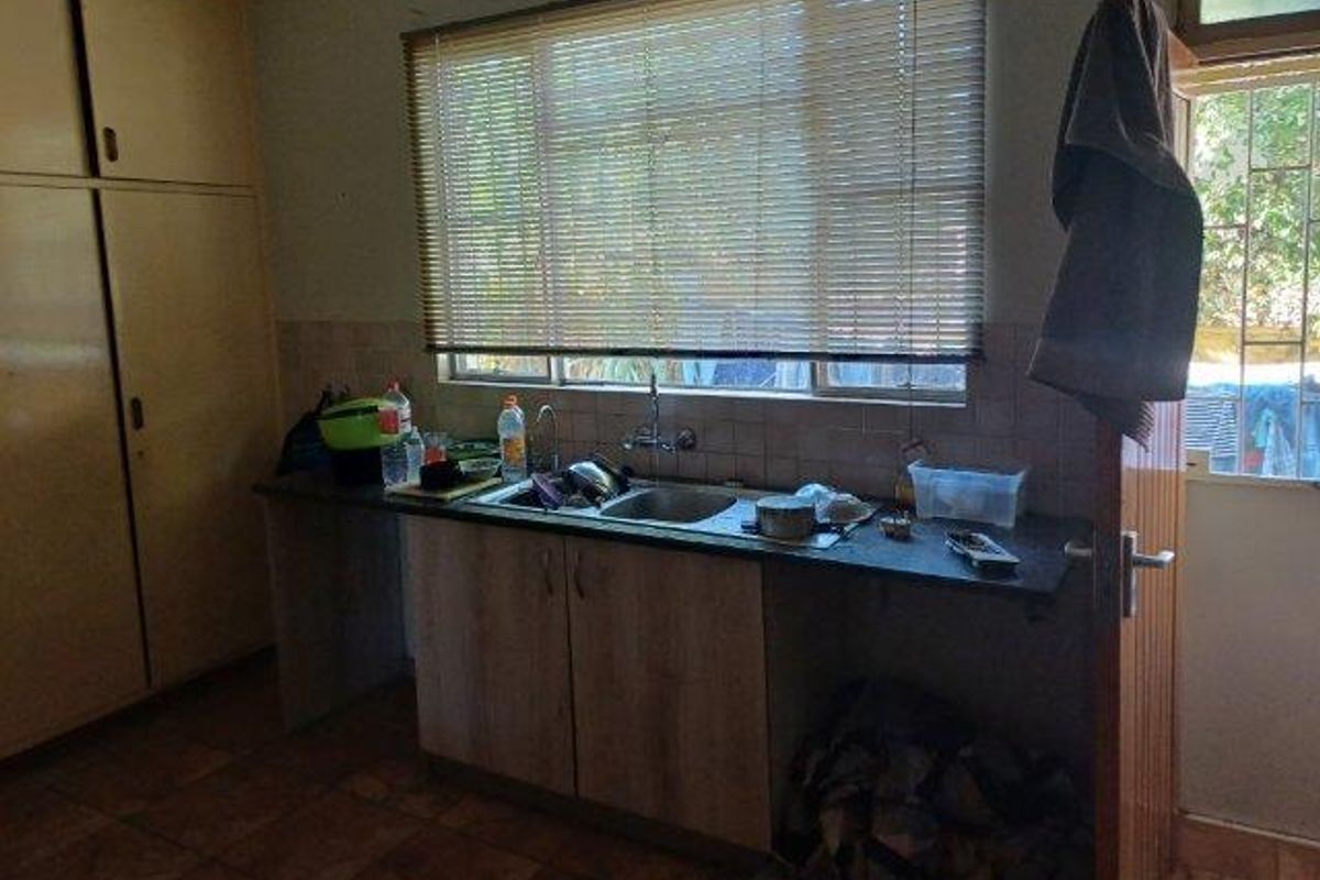 A dated kitchen area featuring built-in cabinetry, a stainless steel sink, and tiled backsplash, offering potential for modernization and renovation.