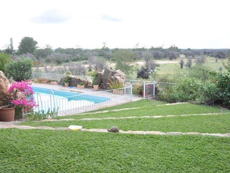 A well-maintained outdoor pool area featuring a swimming pool, safety fencing, and landscaped terraced gardens with scenic views.