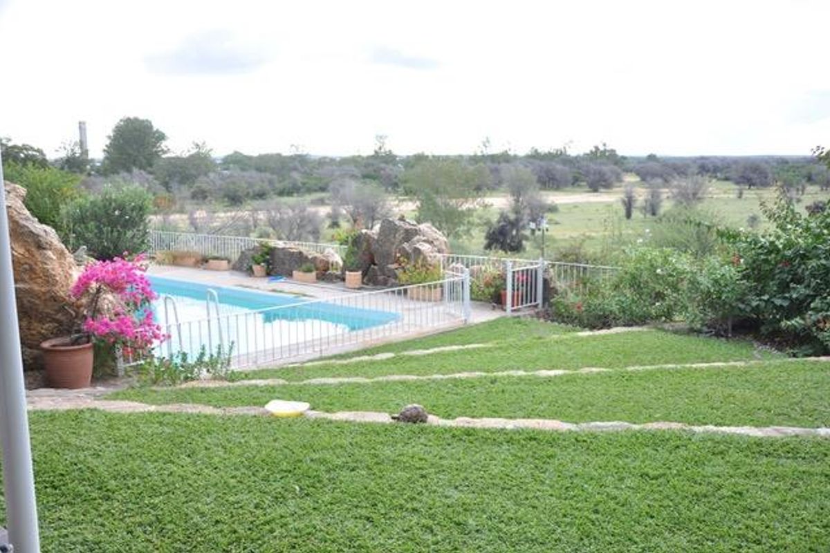 A well-maintained outdoor pool area featuring a swimming pool, safety fencing, and landscaped terraced gardens with scenic views.