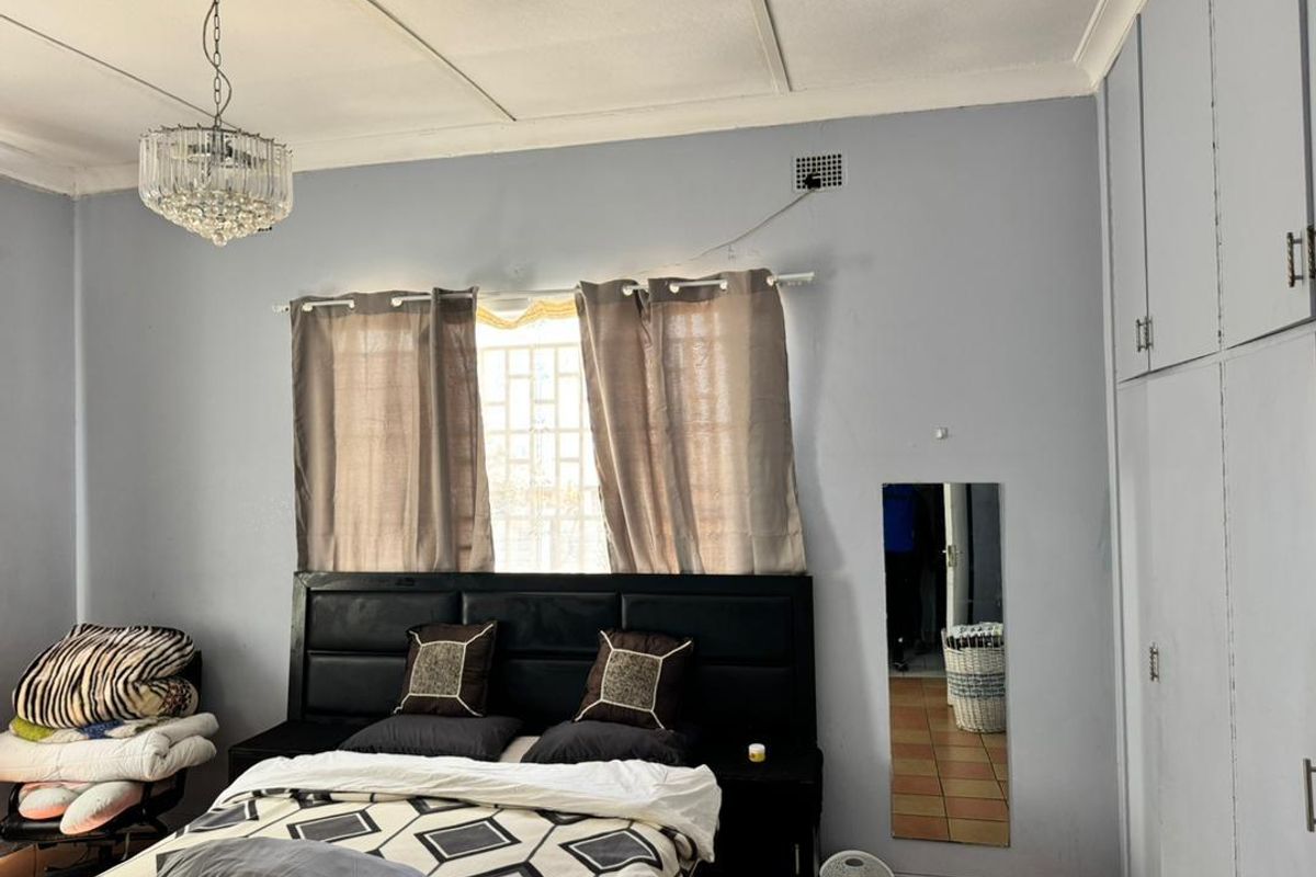 A bedroom featuring built-in cupboards, a ceiling-mounted light fixture, and a window with security bars.