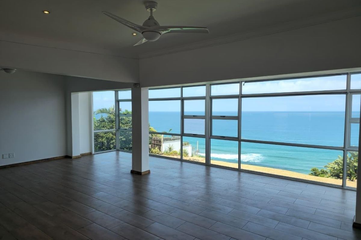 Spacious, empty living area featuring large windows with expansive ocean views, tiled flooring, and a ceiling fan.