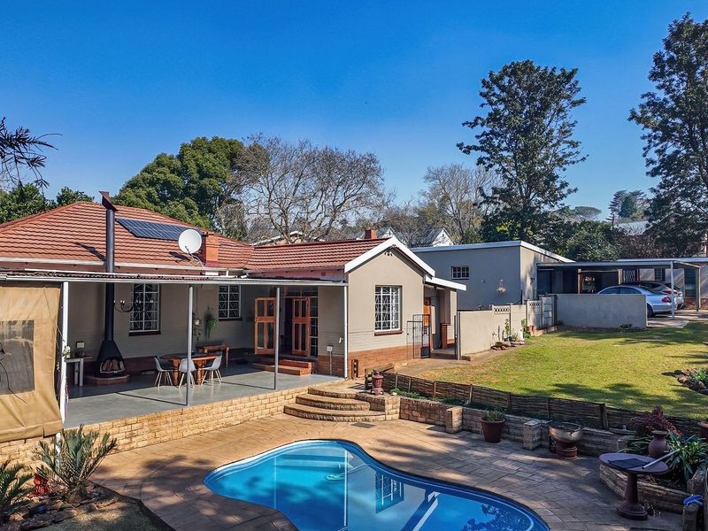 Rear view of the property featuring a swimming pool, covered patio area, landscaped garden, and a detached carport structure.