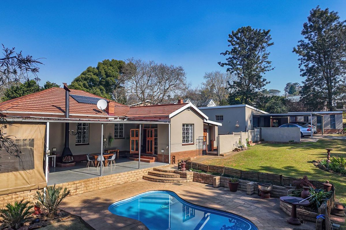 Rear view of the property featuring a swimming pool, covered patio area, landscaped garden, and a detached carport structure.