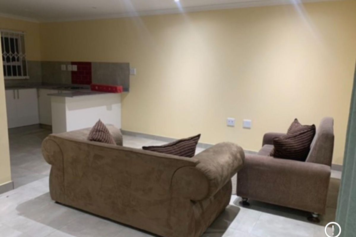 Open-plan living area featuring tiled flooring, recessed lighting, and a compact kitchen with built-in cabinetry and tiled splashback.
