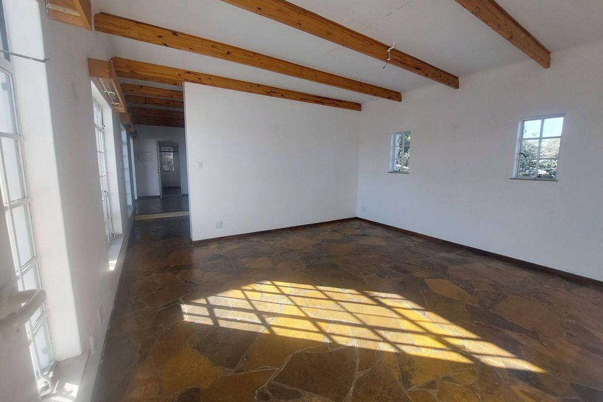 Spacious living area featuring rustic flagstone flooring and exposed timber ceiling beams, offering a bright and open layout.