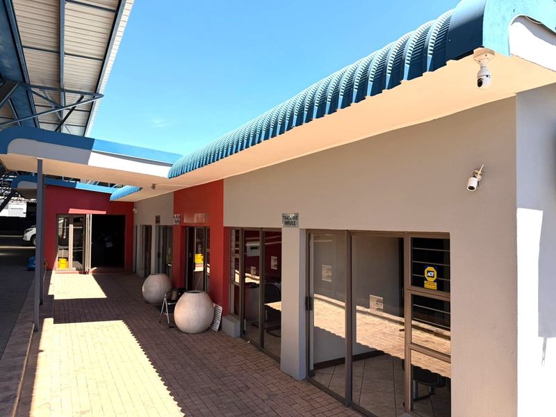 Exterior view of a retail property featuring a paved walkway, curved metal roofing, and multiple glass-fronted commercial units with security systems.
