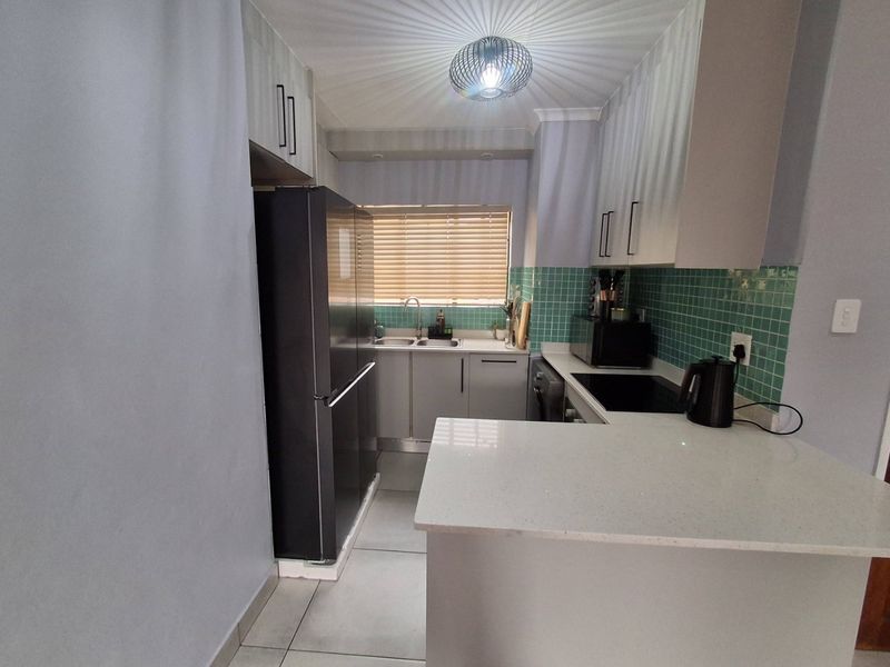 A functional kitchen featuring modern cabinetry, quartz countertops, a tiled backsplash, and a double basin sink, offering a clean and practical workspace.