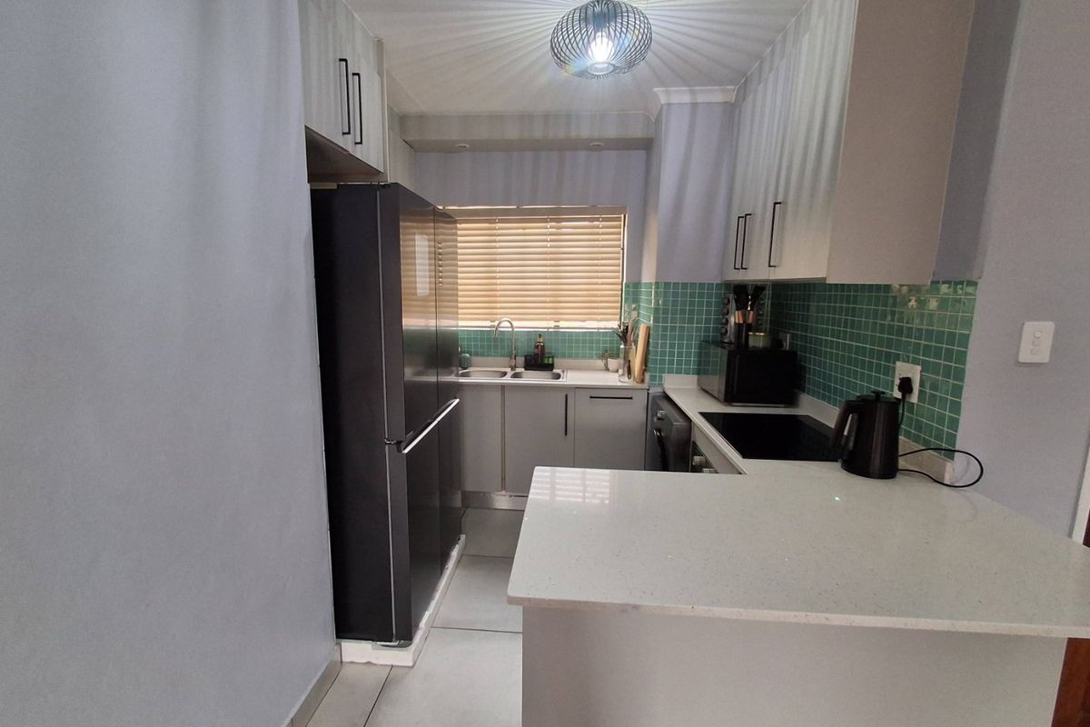 A functional kitchen featuring modern cabinetry, quartz countertops, a tiled backsplash, and a double basin sink, offering a clean and practical workspace.