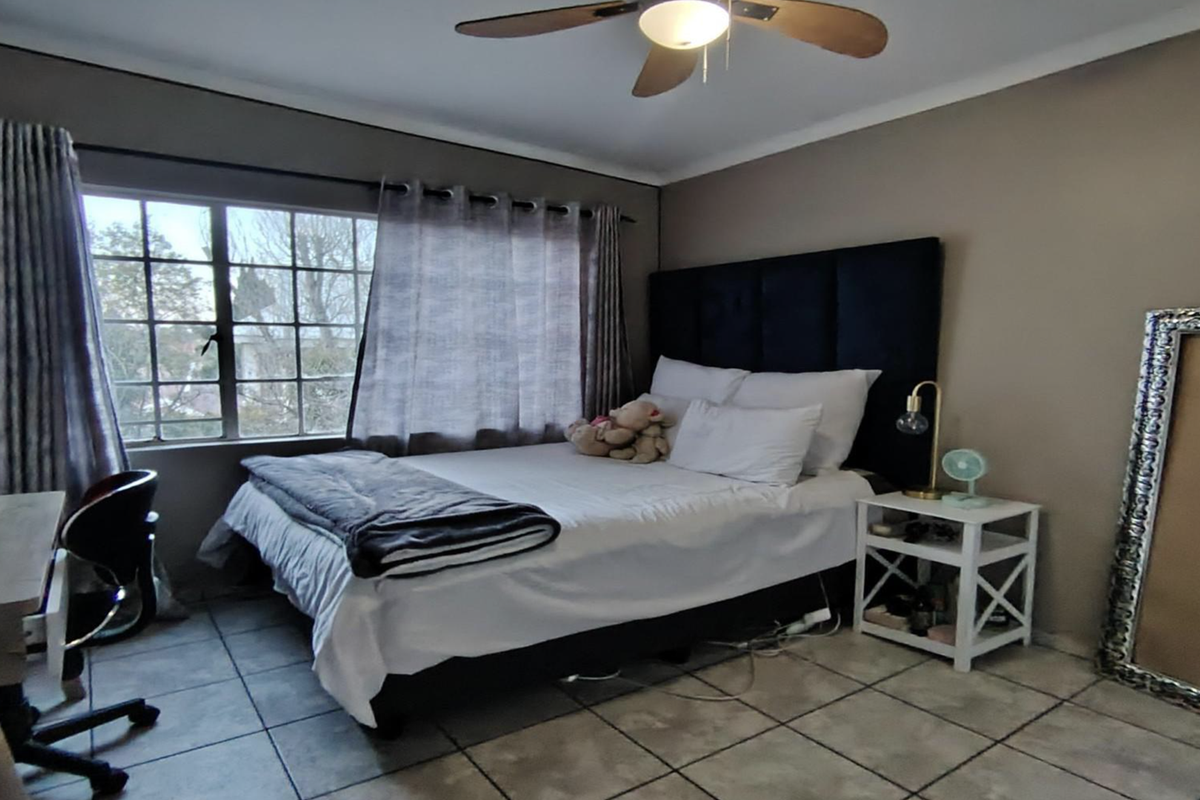 A bedroom featuring tiled flooring, a ceiling fan, and large windows that provide natural light.