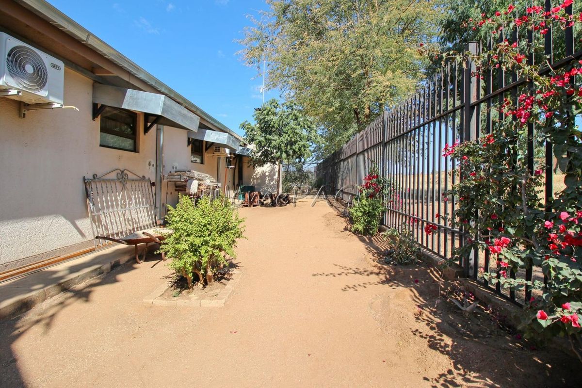 A side exterior view of the property featuring a gravel pathway, metal perimeter fencing, and wall-mounted air conditioning unit.